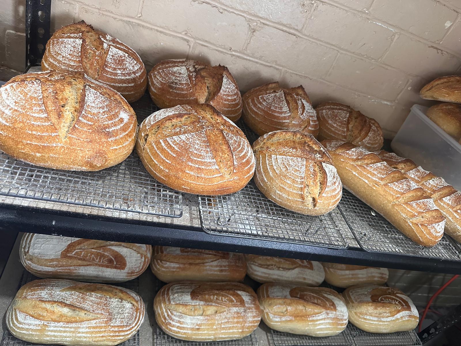 Artisan sourdough loaves cooling on multiple bakery racks during production