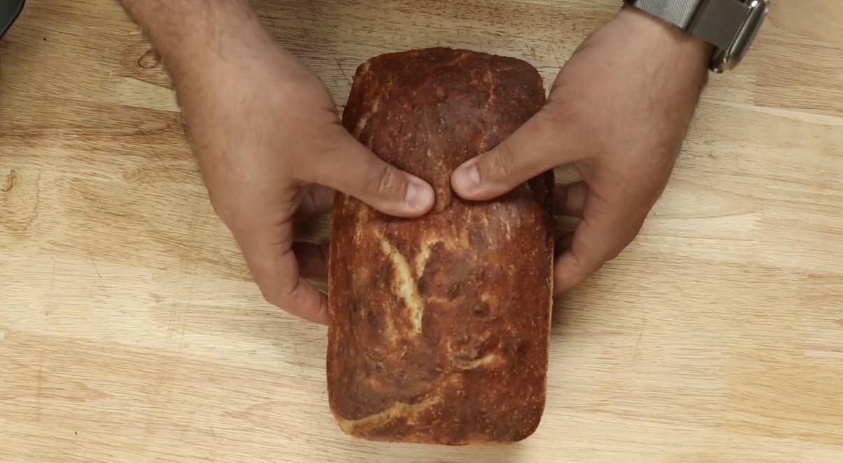 Baker holding a freshly baked golden brown sandwich loaf